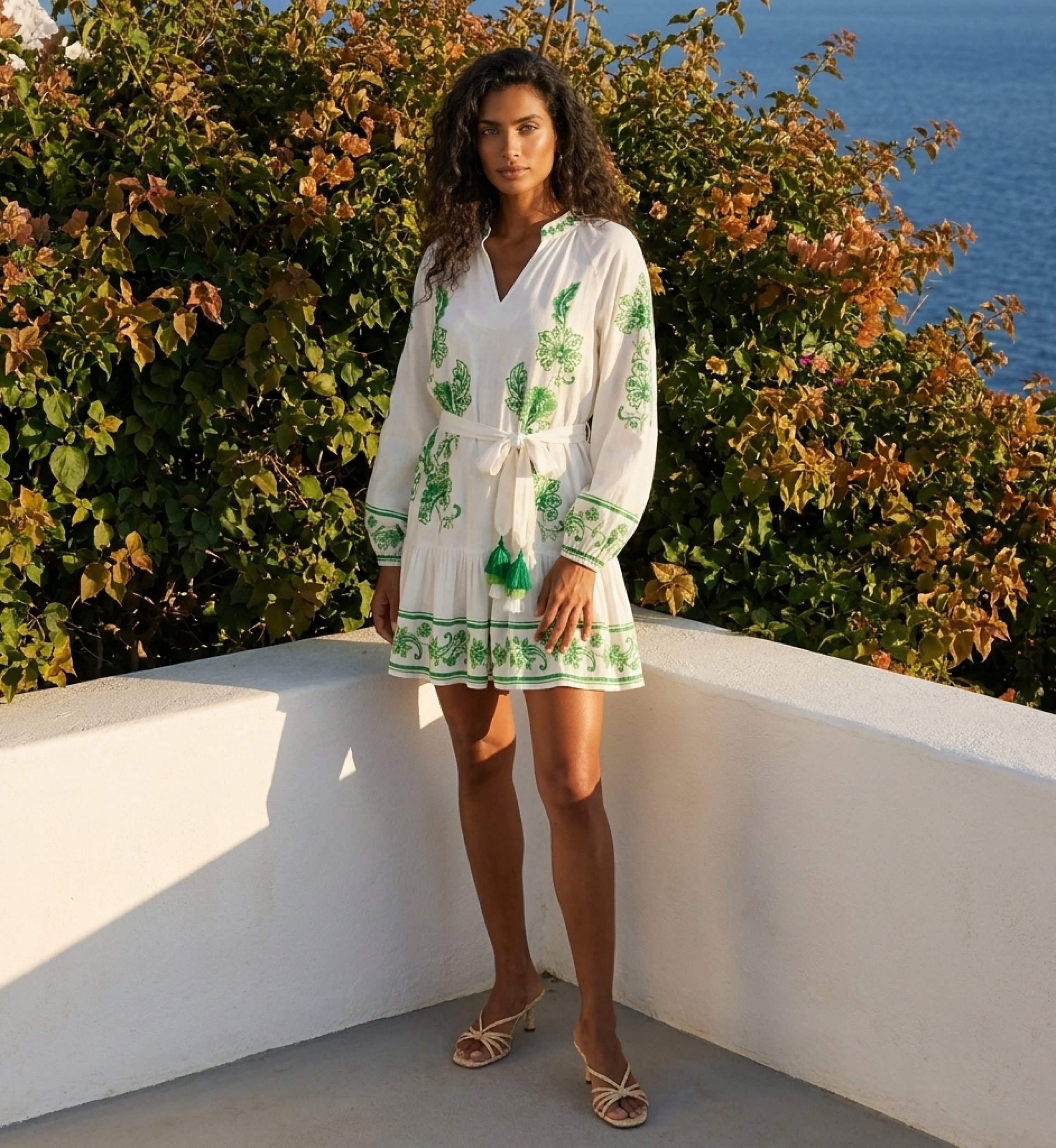 Vestido corto blanco manga larga con bordado floral verde, escote en V, cintura anudada con borlas y falda escalonada.
