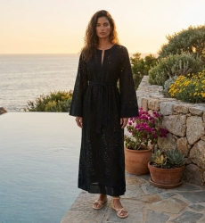Élégante robe longue noire fluide, près d'une piscine à débordement, rochers, coucher de soleil.