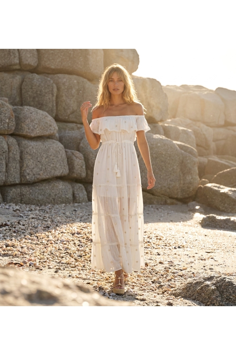 Pink off-shoulder maxi dress with tiered skirt, floral embroidery, and pom-pom trim, sheer lightweight fabric.