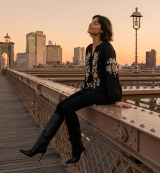 Blouse paysanne noire manches longues, col V à nouer, broderie florale crème, aspect lin, modèle assise au coucher du soleil.