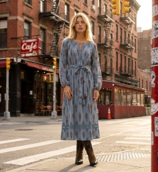 Robe midi bleu clair à motifs floraux rouges et marron, col V, manches longues ballon, taille nouée à pompons, vue urbaine.