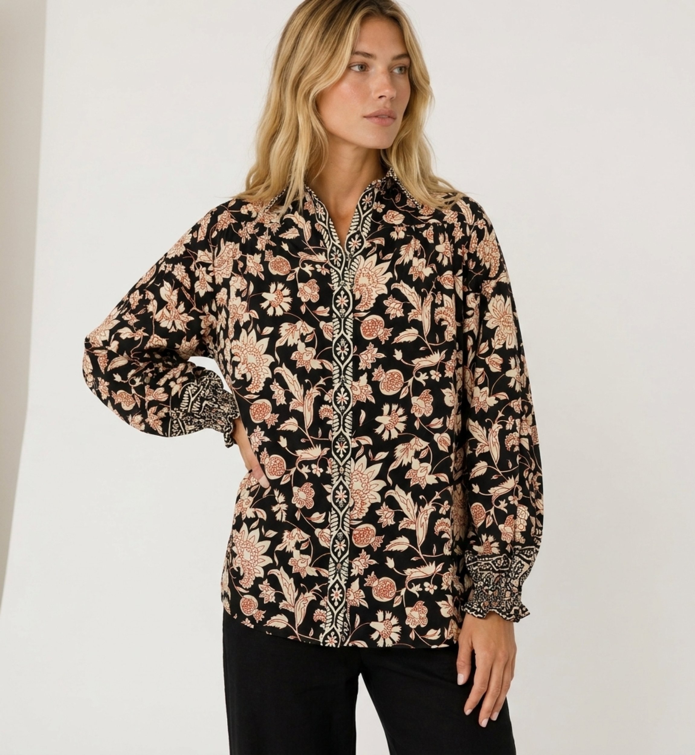 Blouse noire à manches longues, motif floral crème et rouille, col et poignets volantés en tissu léger.