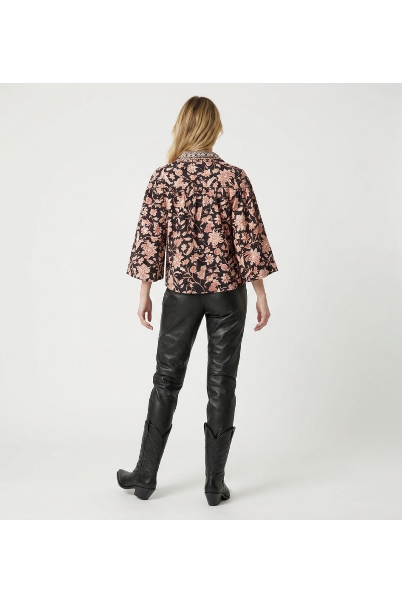 Blusa negra manga larga floral, estampado crema y óxido, cuello, puños con volantes, tela ligera, vista trasera.