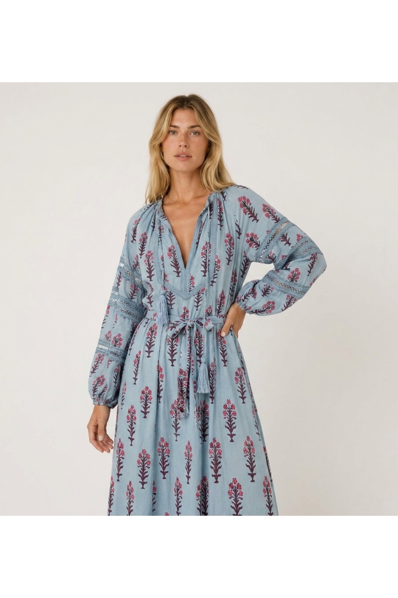 Robe midi fleurie bleu clair, vue trois quarts. Manches longues ballon, col en V, taille nouée à pompons.