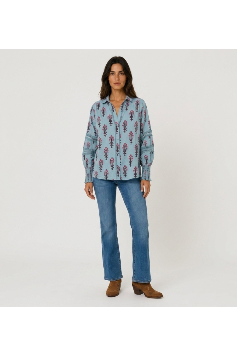Camisa azul claro floral con botones, cuello V, mangas abullonadas con encaje y puños fruncidos. Vista frontal.