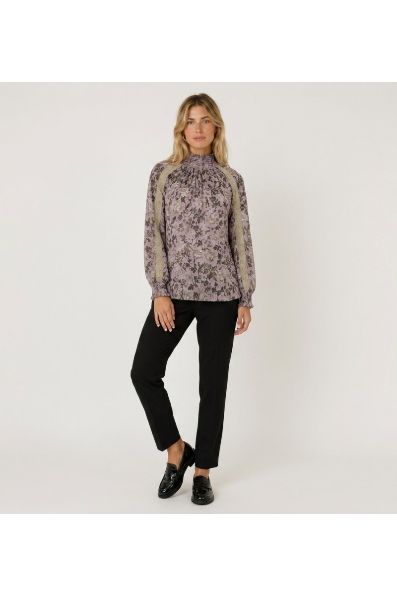 Blouse violette à manches longues et col montant, motif floral sombre, dentelle beige et poignets smockés, vue de face.