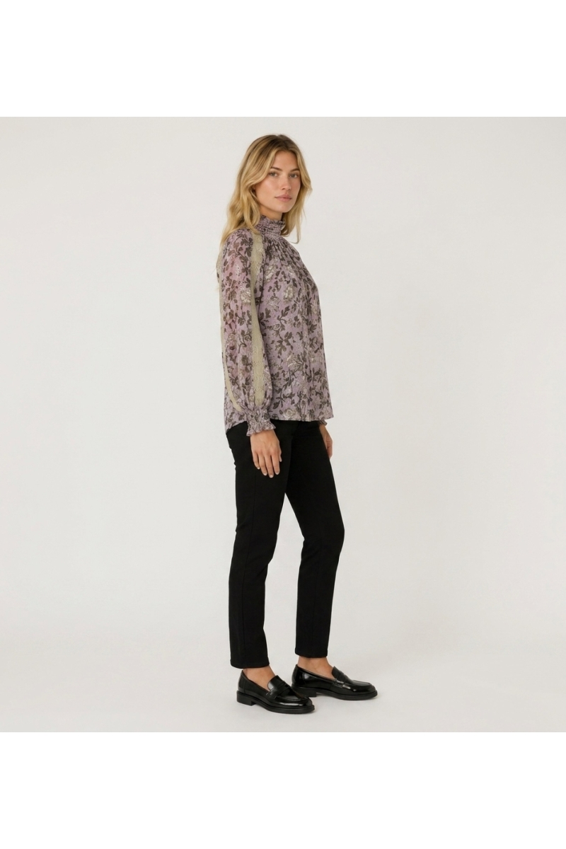 Vue trois-quarts d'une blouse violette à manches longues, col montant, motif floral sombre, dentelle beige et poignets smockés.