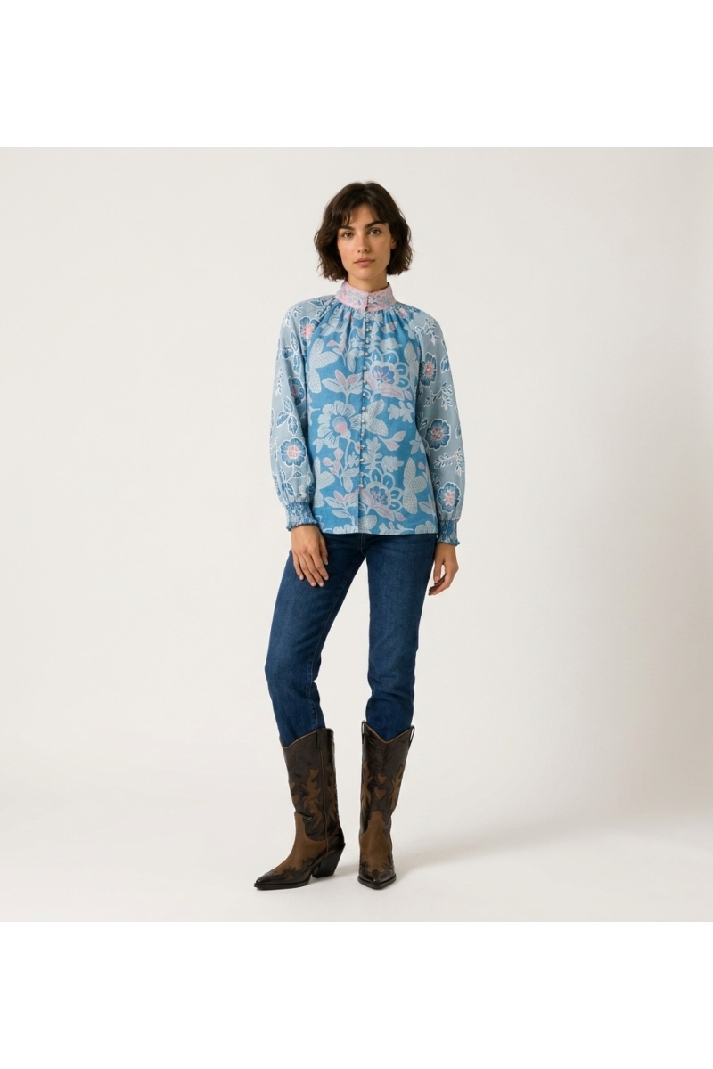 Vista frontal de blusa azul de manga larga con estampado floral rosa y blanco, cuello alto y corte holgado.