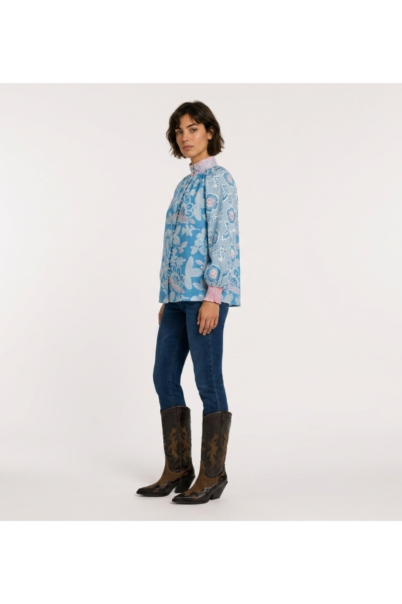 Blusa azul manga larga con estampado floral rosa y blanco, cuello alto, corte holgado, tela tipo algodón, vista de 3/4.
