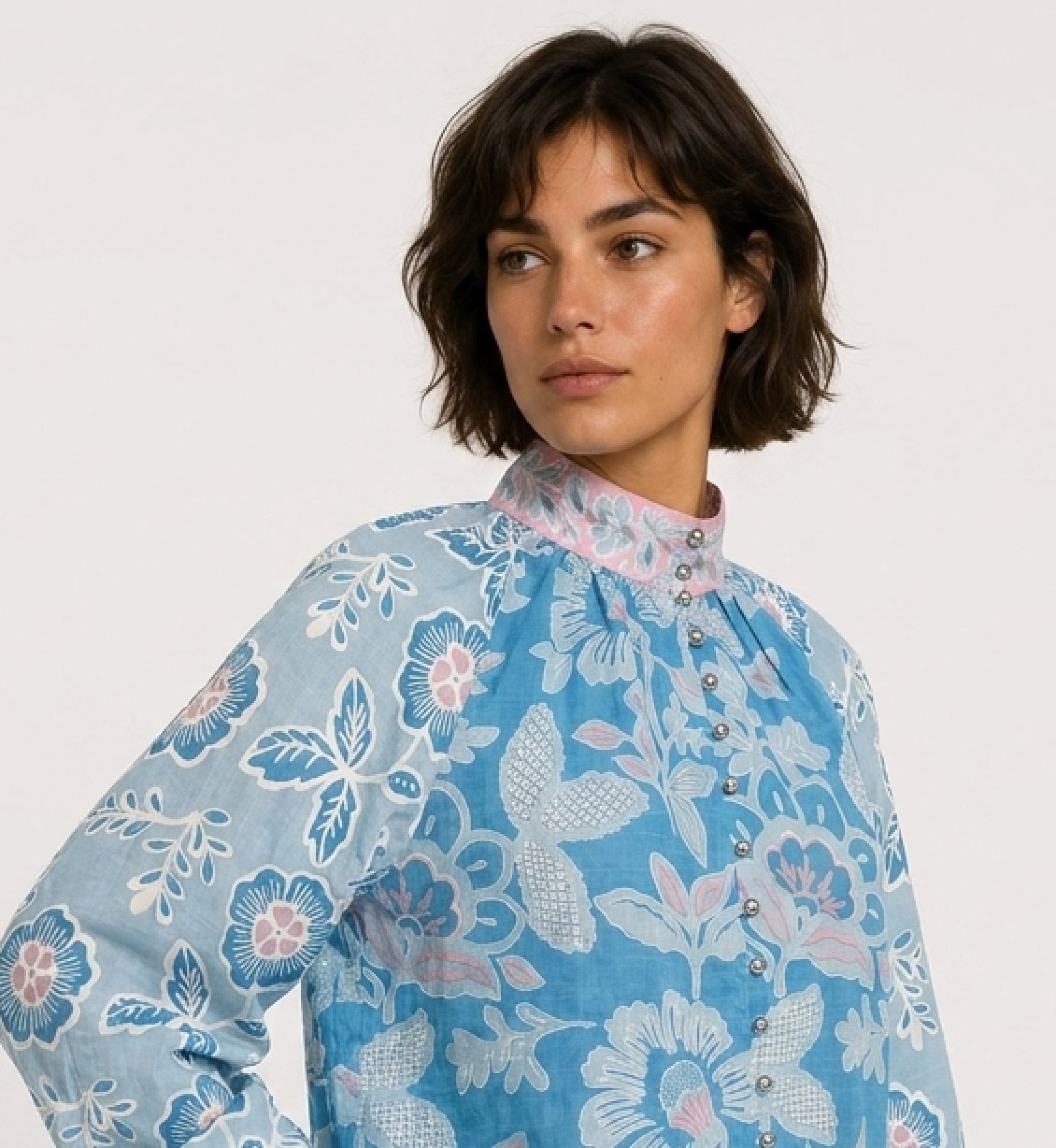 Chemisier bleu à manches longues, motifs floraux roses et blancs, col montant, coupe ample en tissu coton, vue de trois-quarts.