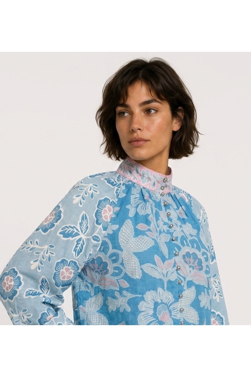 Blusa azul de manga larga con estampado floral rosa y blanco, cuello alto y corte holgado de tela tipo algodón, vista lateral.