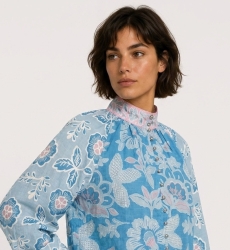 Three-quarter side view of a blue long-sleeve floral blouse with pink and white patterns, high neck, and loose fit in soft cotto