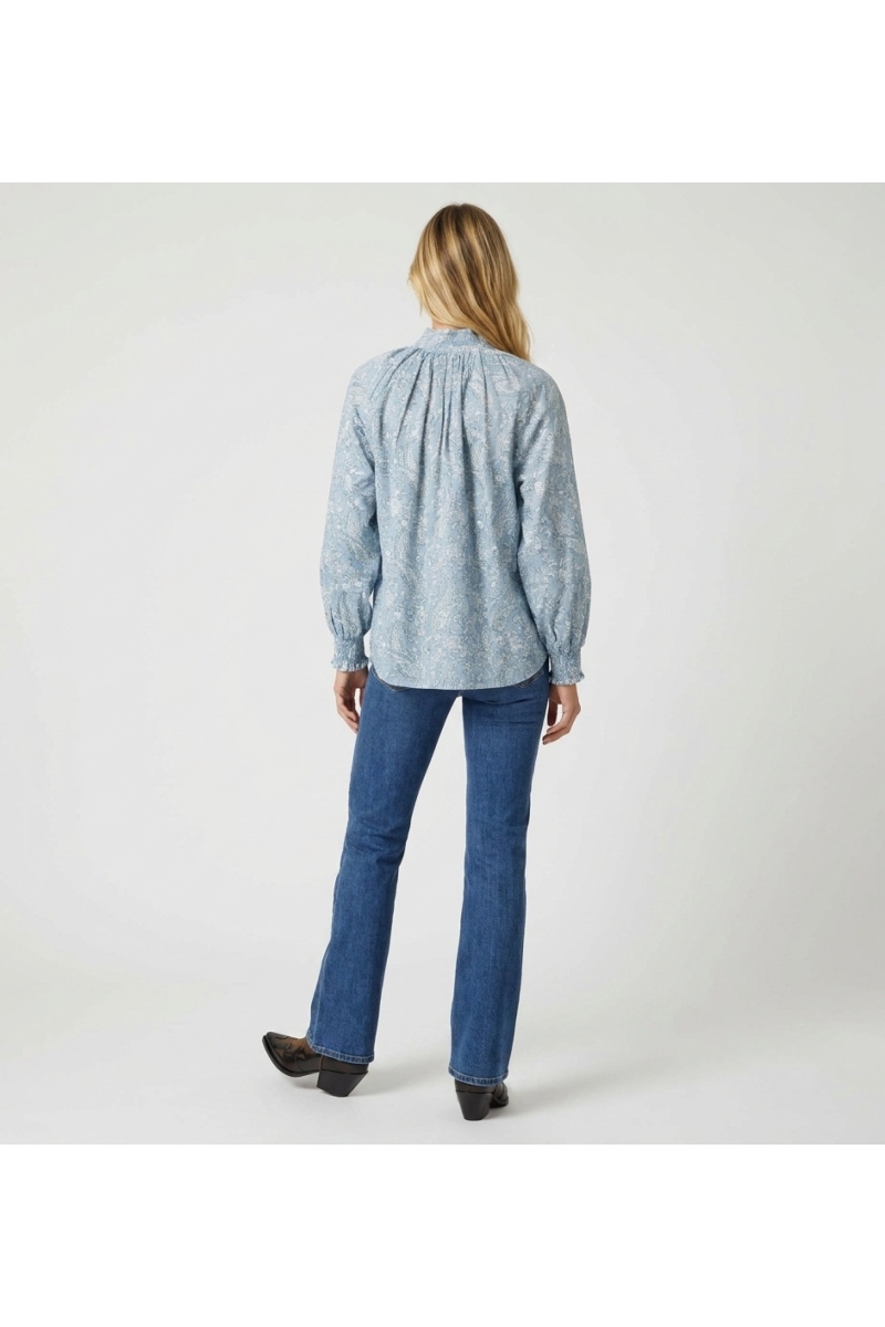 Blusa azul claro de manga larga con estampado cachemir blanco, cuello alto, puños con volantes, vista trasera. Camisa elegante.