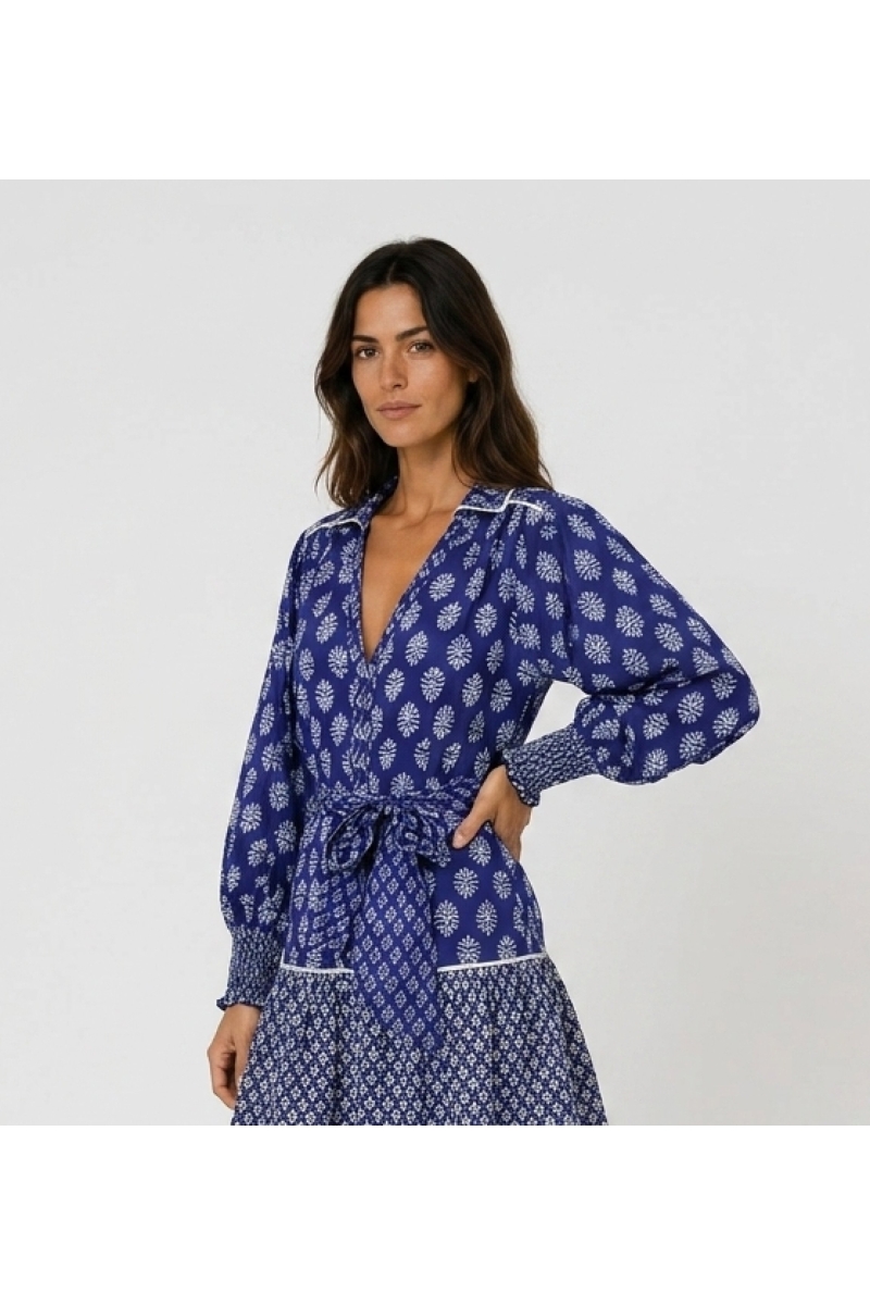 Vue trois-quarts : blouse bleue à motif floral, col en V, manches longues, poignets smockés, tissu léger.