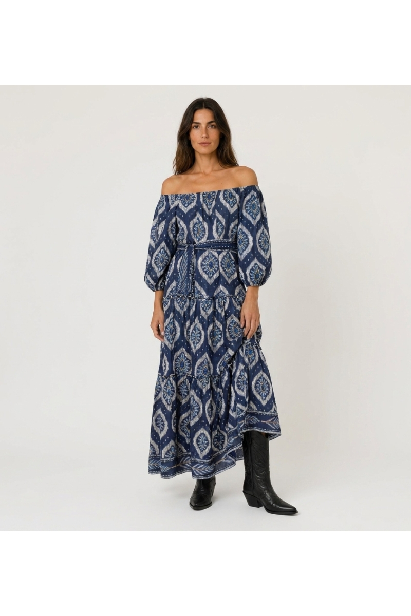 Robe longue marine à épaules dénudées, motif ikat blanc/bleu clair, volants, manches bouffantes et ceinture nouée.
