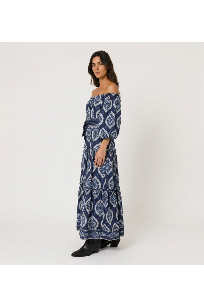 Vestido maxi azul marino escalonado, hombros descubiertos, estampado ikat blanco, mangas abullonadas, cinturón.