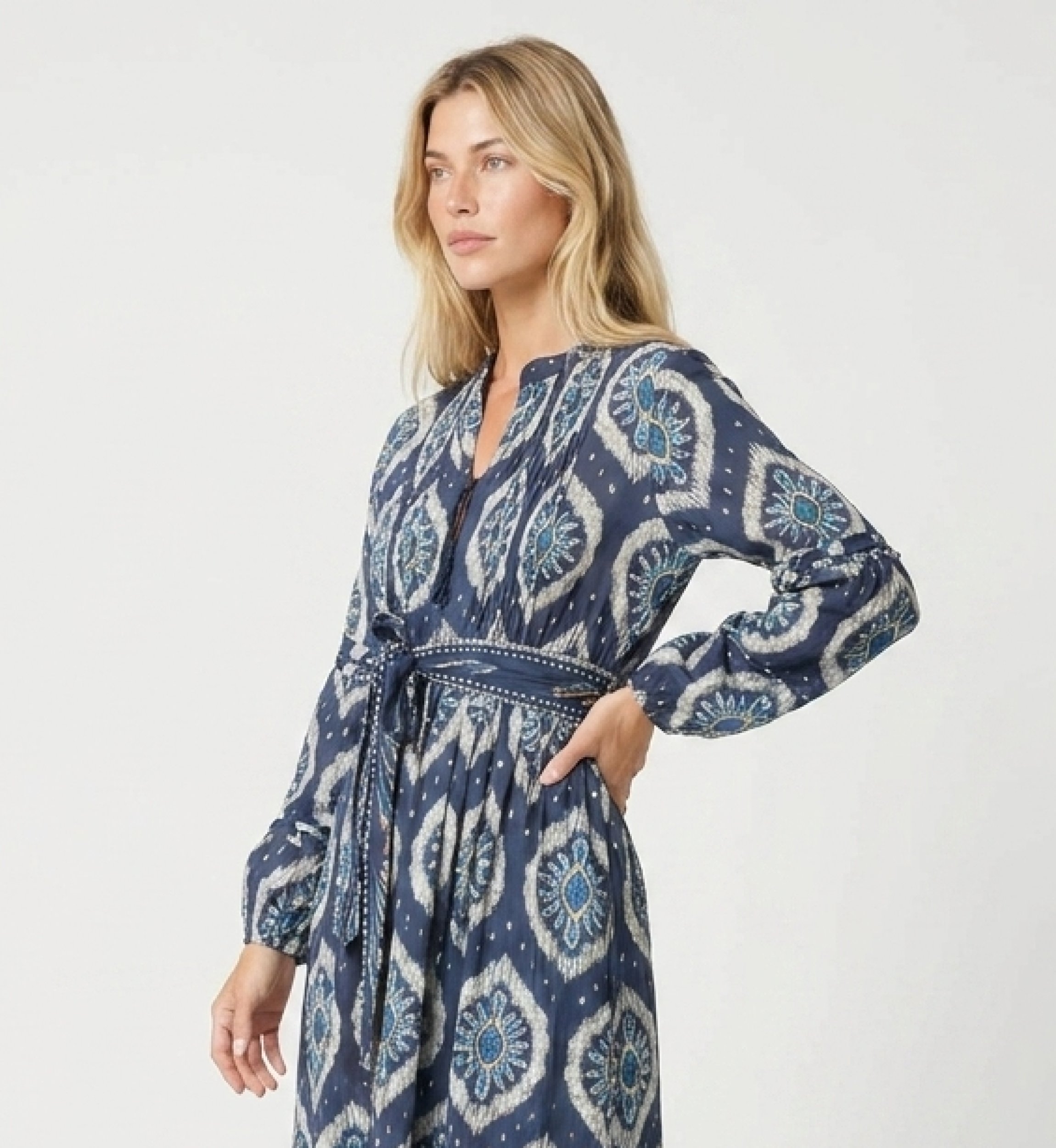 Vista tres cuartos de vestido midi ikat azul y blanco con mangas abullonadas, falda escalonada y cinturón.