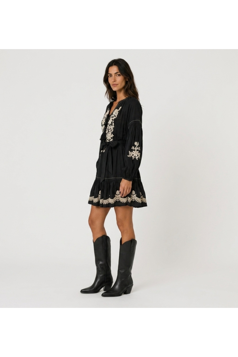 Black loose fit mini dress, long balloon sleeves, tiered skirt, white floral embroidery, tie-waist. Side view.