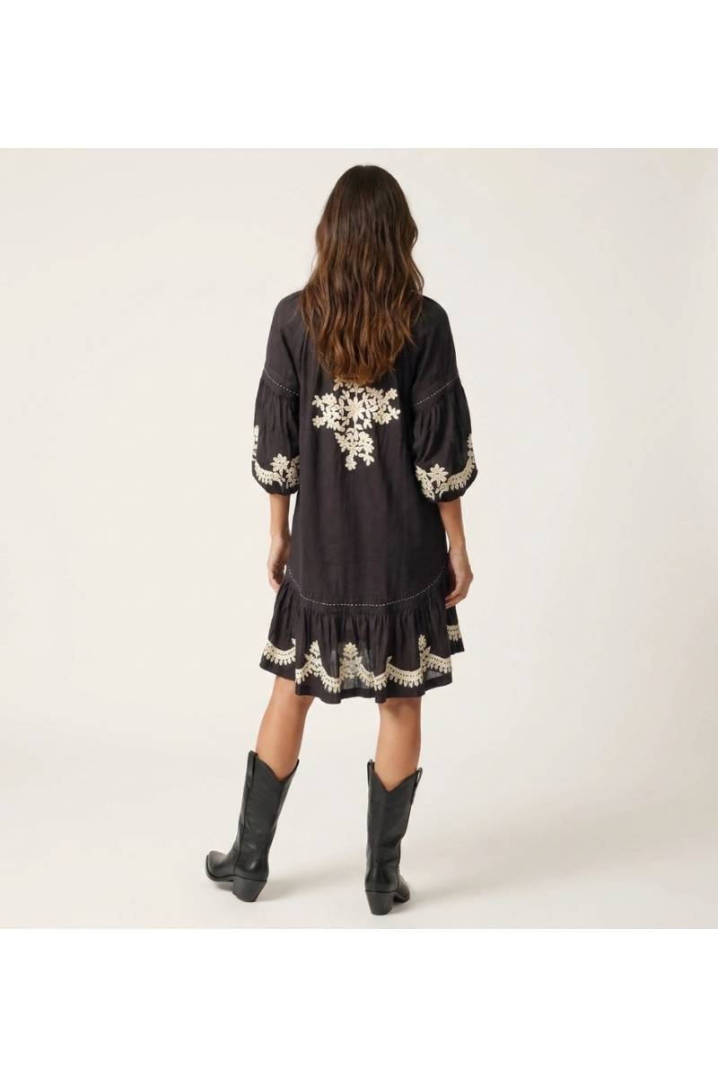 Robe courte noire ample, manches ballon longues, jupe à volants, broderie florale blanche, taille nouée, vue dos.