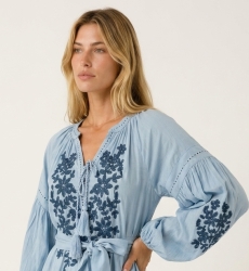 Robe courte noire ample, manches ballon longues, jupe à volants, broderie florale blanche, taille nouée, vue de trois-quarts.