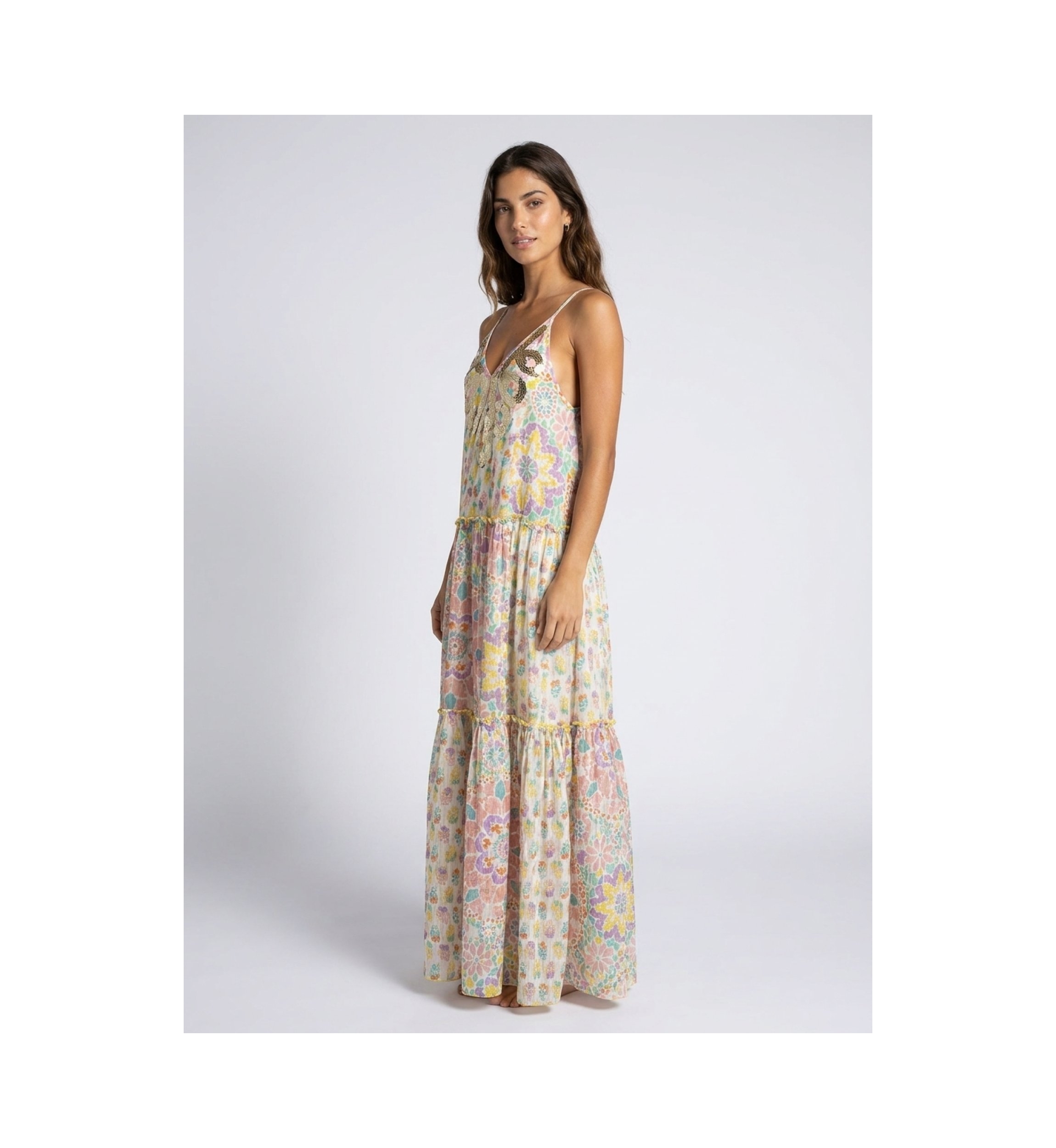 Vestido largo maxi blanco con volantes, tirantes finos, escote V con lentejuelas oro/plata, estampado floral, modelo de lado.